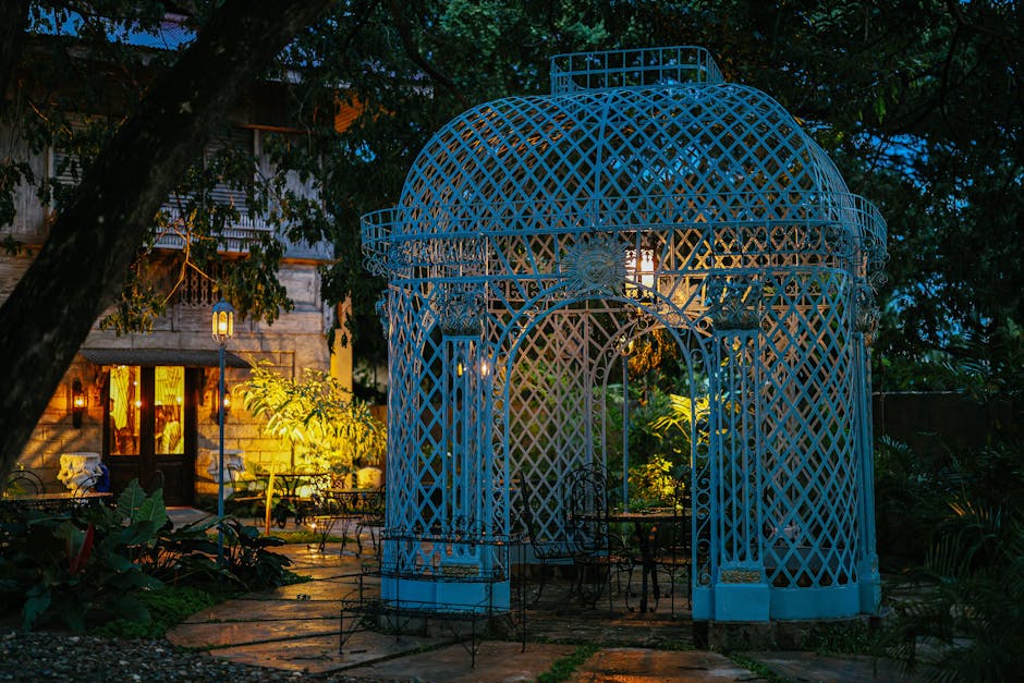 A vintage blue gazebo lit up in a lush garden setting during twilight, offering a serene and picturesque scene.